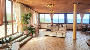 A spacious living room with a large window overlooking the sea, a wooden ceiling, and a beige sofa. - Lovely home in Caronia (Caronia)
