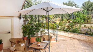 An outdoor patio with wicker furniture, a table, and a large umbrella. - Lovely home in Caronia (Caronia)