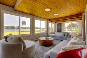 Un salón amplio con un ventanal grande, techo de madera y vista a un lago.
