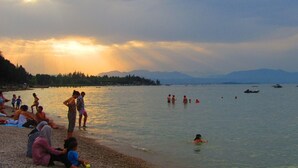 A beach scene with people relaxing and swimming, surrounded by mountains and boats in the water. - Near Gardaland, 2 minutes from the lake, in the heart of Peschiera del Garda! Xenia19 (Peschiera del Garda)