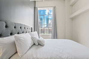 A neatly made bed with a tufted headboard, white bedding, and a window with curtains.
