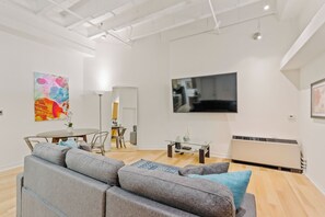 A modern living room with a grey sofa, a coffee table, a flat-screen TV, and a painting on the wall.