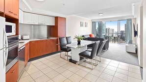 A modern kitchen with stainless steel appliances, a dining area with a glass table, and a balcony with a city view. - Chevron Renaissance Ocean View (Surfers Paradise)