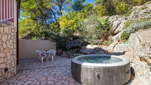 A stone patio with a hot tub, a table with chairs, and a view of a rocky hillside with trees. - Pet friendly apartment in Stasevica (Stasevica)