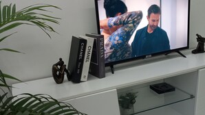 A flat-screen TV on a white entertainment unit with books and a figurine.