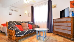 Een woonkamer met een bank, een klein rond tafeltje, een dressoir en een televisie.