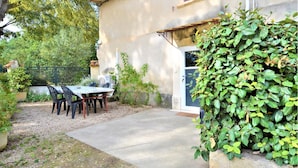 Een terras met tafel en stoelen, een kleine tuin en een gebouw met een deur en raam.