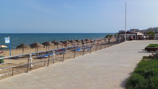 Una passeggiata lungomare con file di ombrelloni di paglia, un percorso pedonale e vista sul mare.