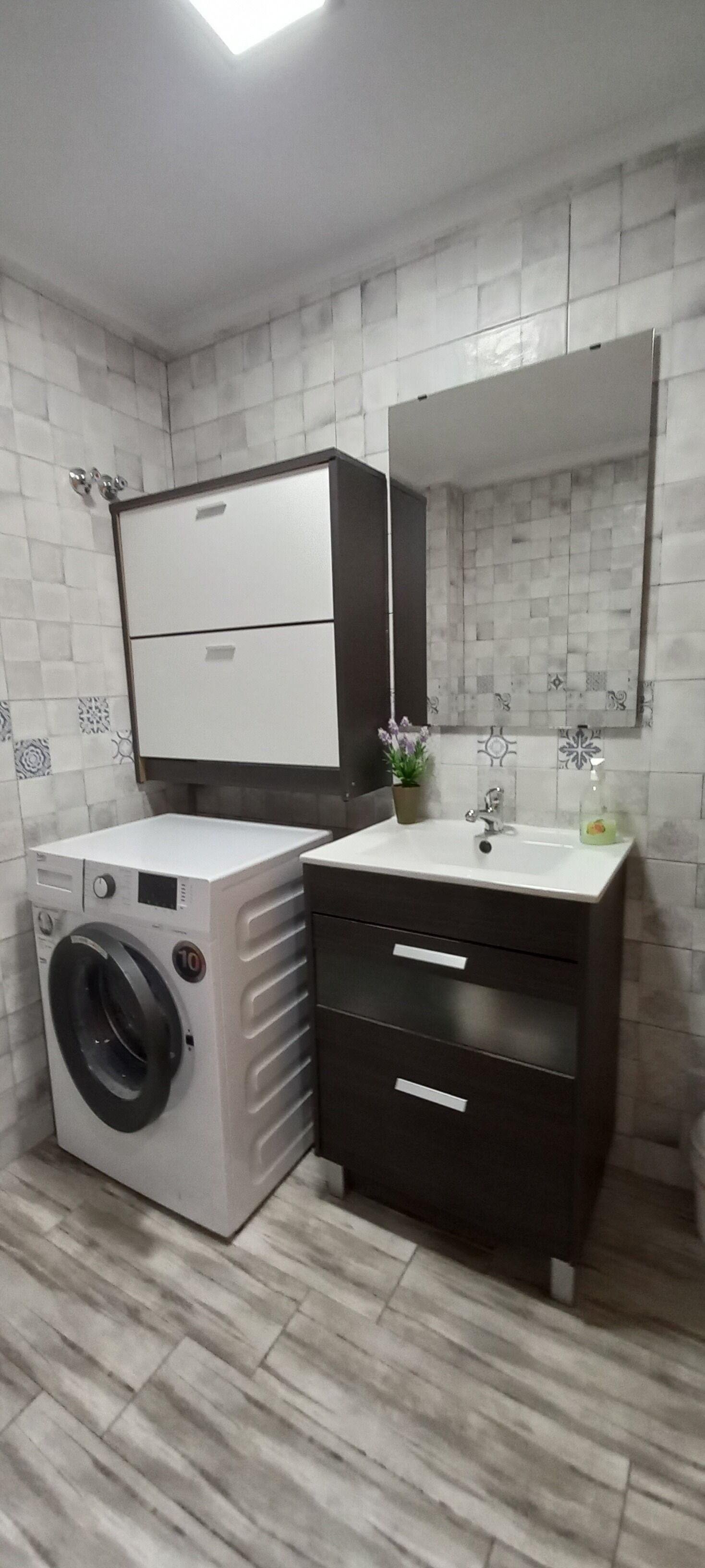 A compact bathroom with a washing machine, a sink, and a dark cabinet with drawers.