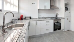 A modern kitchen with white cabinets, a stainless steel sink, a microwave, and an oven. - Gorgeous apartment in Grau i Platja with WiFi (Grau i Platja)