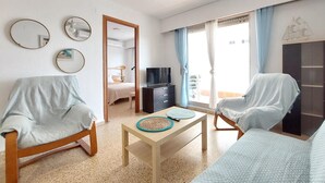 A room with two armchairs, a small table, a bed, a TV, and a sliding door leading to a balcony. - Gorgeous apartment in Grau i Platja with WiFi (Grau i Platja)