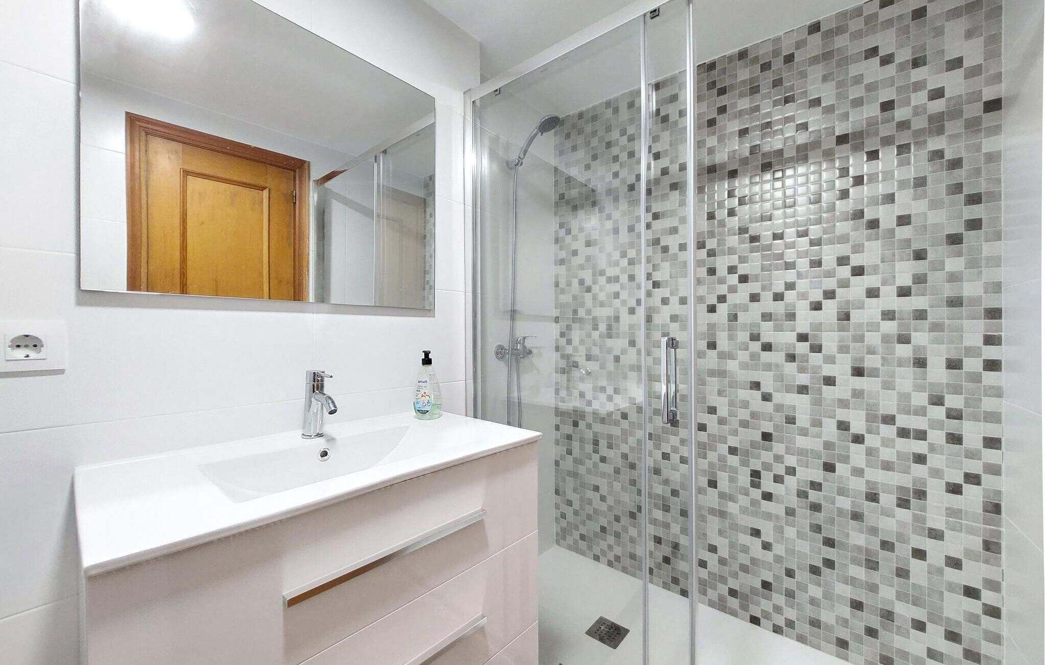 A modern bathroom with a glass-enclosed shower, a white sink, and a tiled backsplash.