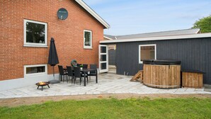 Ein Backsteinhaus mit einer Terrasse, auf der sich ein Tisch, Stühle, ein Whirlpool und eine Feuerstelle befinden.