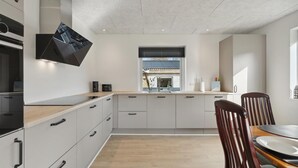 Eine moderne Küche mit Einbauofen, Fenster mit Blick und Essbereich mit Tisch und Stühlen.