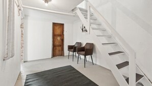 Eine Treppe mit weißen Geländern führt zu einer oberen Etage, ein Holztür und zwei Stühle in einem Flur mit dunklem Teppich.