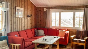 A cozy room with a red sofa, a wooden table, and a chair. There is a window with a view of a snowy landscape. - 3 bedroom lovely home in Hemsedal (Hemsedal)