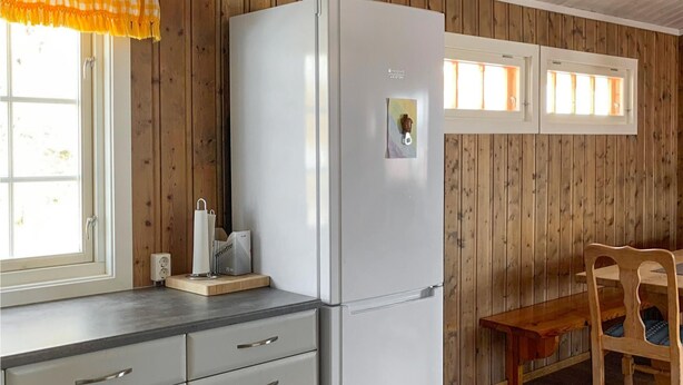 A kitchen with a white refrigerator, wooden panel walls, a window with a yellow checkered curtain, a wooden table, and a chair. - 3 bedroom lovely home in Hemsedal (Hemsedal)