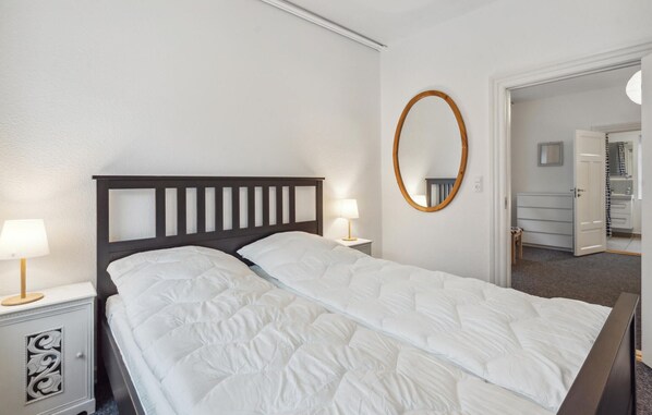 Una cama bien hecha con cabecera de madera, una lámpara de noche y un espejo redondo en la pared.