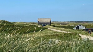 Un paysage rural avec une seule maison sur une colline herbeuse, un chemin menant à cette maison et un panneau indiquant que l’accès aux tracteurs y est interdit.