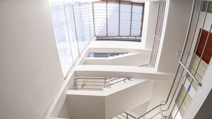 Un interior de varios niveles con una escalera central, barandillas de vidrio y un extintor en la planta baja.