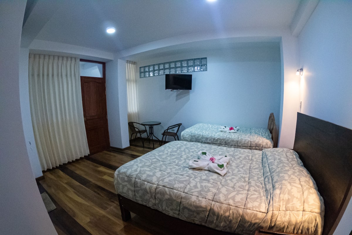 A hotel room with two beds, a small table, chairs, a TV, and a window with curtains.