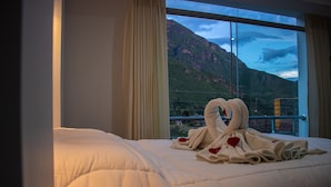 Habitación de hotel con una cama grande, vista de montañas a través de una ventana y una presentación de toallas en la cama.