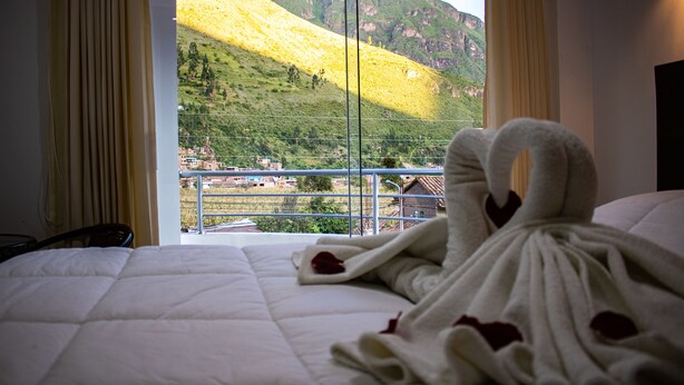 Una habitación de hotel con cama, ventana con cortinas y vista a la montaña.