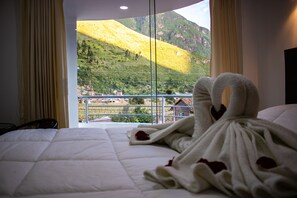 A hotel room with a bed, a window with curtains, and a view of a mountain. - Hotel Los Laureles (Calca)