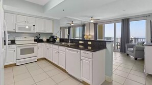 A modern kitchen with white cabinets, a central island, and a view to the balcony. - BEAUTIFUL GULF VIEWS, 4 MIN WALK to BEACH  MANY UPGRADES SUNSETS ARE AWESOME (Miramar Beach)