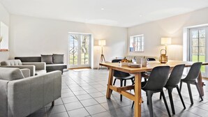 A spacious living room with a grey sofa set, a wooden dining table with chairs, and a large window providing natural light. - 4 bedroom lovely home in Næstved (Næstved)
