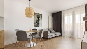 A modern living room with a dining area, featuring a round table, grey chairs, a grey sofa, and a large window with sheer curtains. - 2 bedroom lovely apartment in Gdynia (Gdynia)