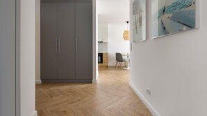 A hallway with a grey wardrobe, a dining area with a table and chairs, and a painting on the wall. - 2 bedroom lovely apartment in Gdynia (Gdynia)