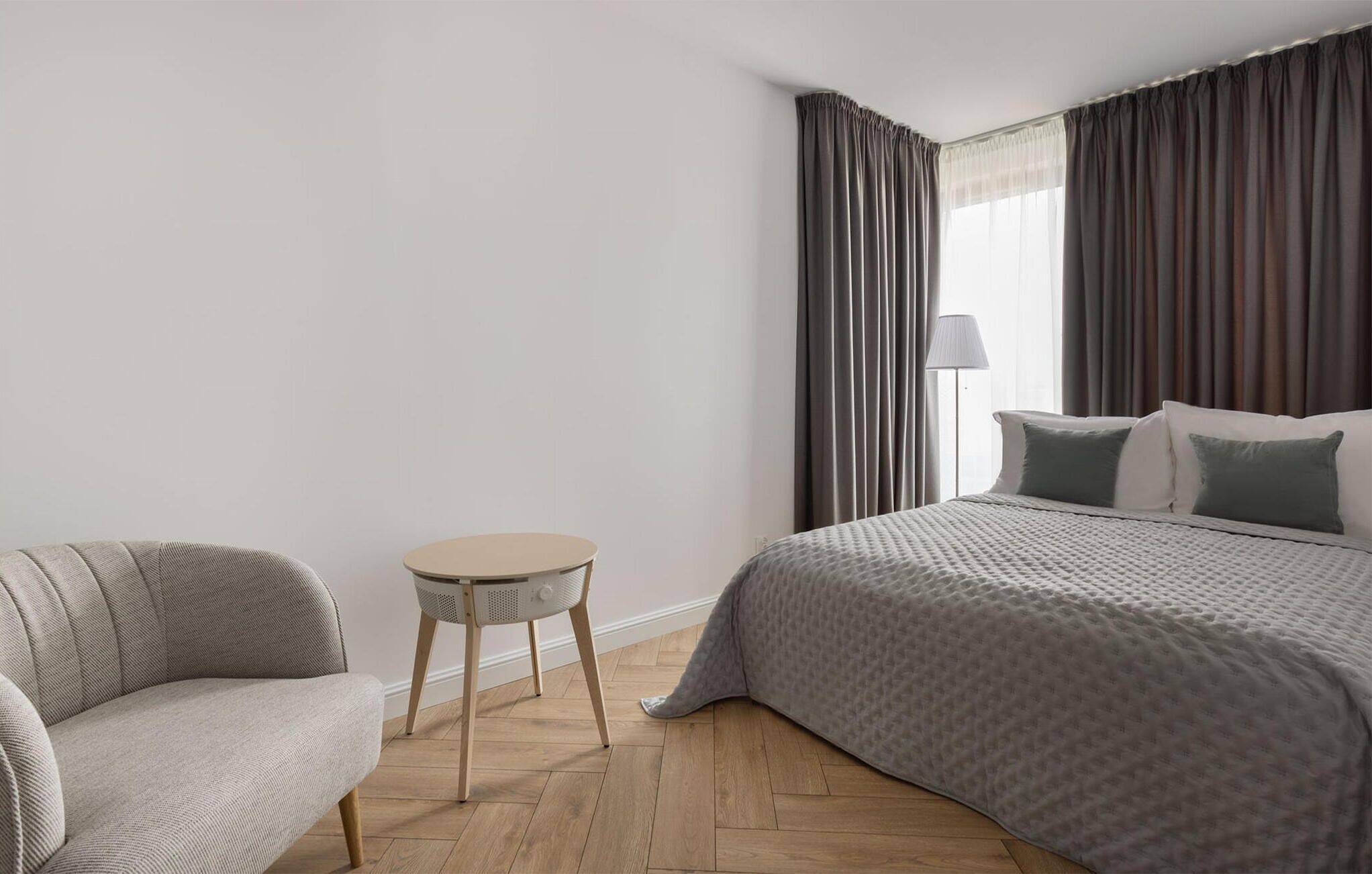 Et hotelværelse med en seng, en stol, et rundt bord og en lampe.