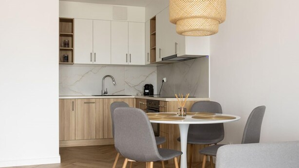 A modern kitchen with white cabinets, a marble backsplash, and a round dining table with grey chairs. - 2 bedroom lovely apartment in Gdynia (Gdynia)