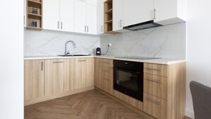 A modern kitchen with wooden cabinets, a marble countertop, a stainless steel faucet, and a built-in oven. - 2 bedroom lovely apartment in Gdynia (Gdynia)