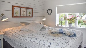Un dormitorio con una cama, dos lámparas de noche, un ventanal con vistas y una planta en la pared.