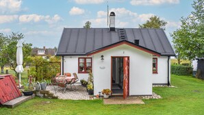 Una casa pequeña y blanca con una puerta roja, un patio con mesa y sillas, y un jardín.