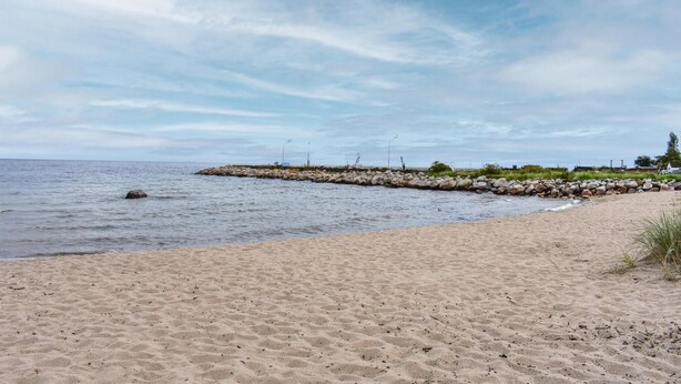 Una playa arenosa con un rompeolas rocoso y agua tranquila.