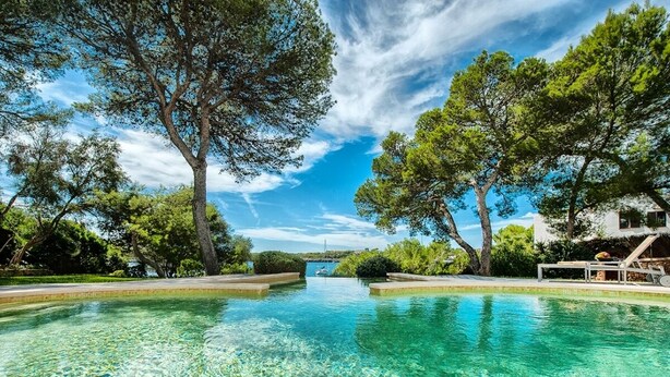 Piscina límpida cercada por árvores e um edifício branco com varanda.