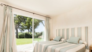 Quarto com duas camas, uma janela grande e vista para um jardim.