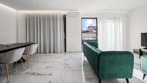 A modern living room with a dining area, featuring a marble floor, green upholstered sofa, and a view of a construction site through a glass door. - Beach front home in Vodice (Vodice)