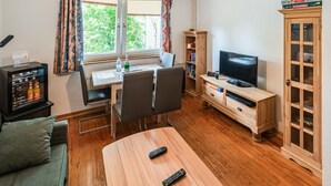 A cozy living room with a wooden dining table, two chairs, a TV, a bookshelf, and a cabinet.