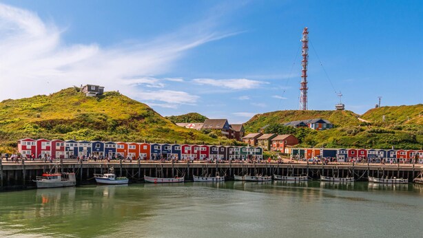A coastal town with colorful houses, a dock with boats, and a hill with a building.