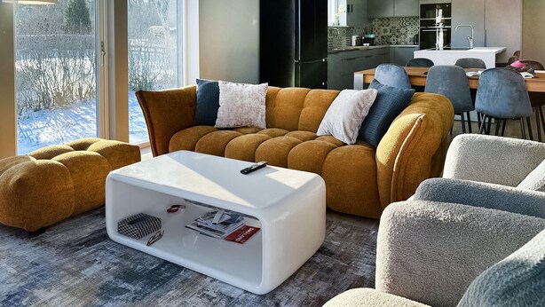 A living room with a sofa, ottoman, and a white coffee table with a remote control.
