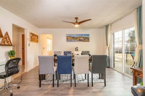 Comedor con una mesa dispuesta para cuatro, ventilador de techo y una ventana grande con cortinas.