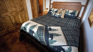 Un dormitorio con estructura de cama de madera, colcha acolchada con estampados de animales y armario de madera.