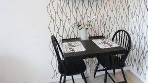 A small dining area with a table and two chairs, a vase with flowers, and a wall with a geometric pattern. - Cozy apartment in Gdynia with WiFi (Gdynia)