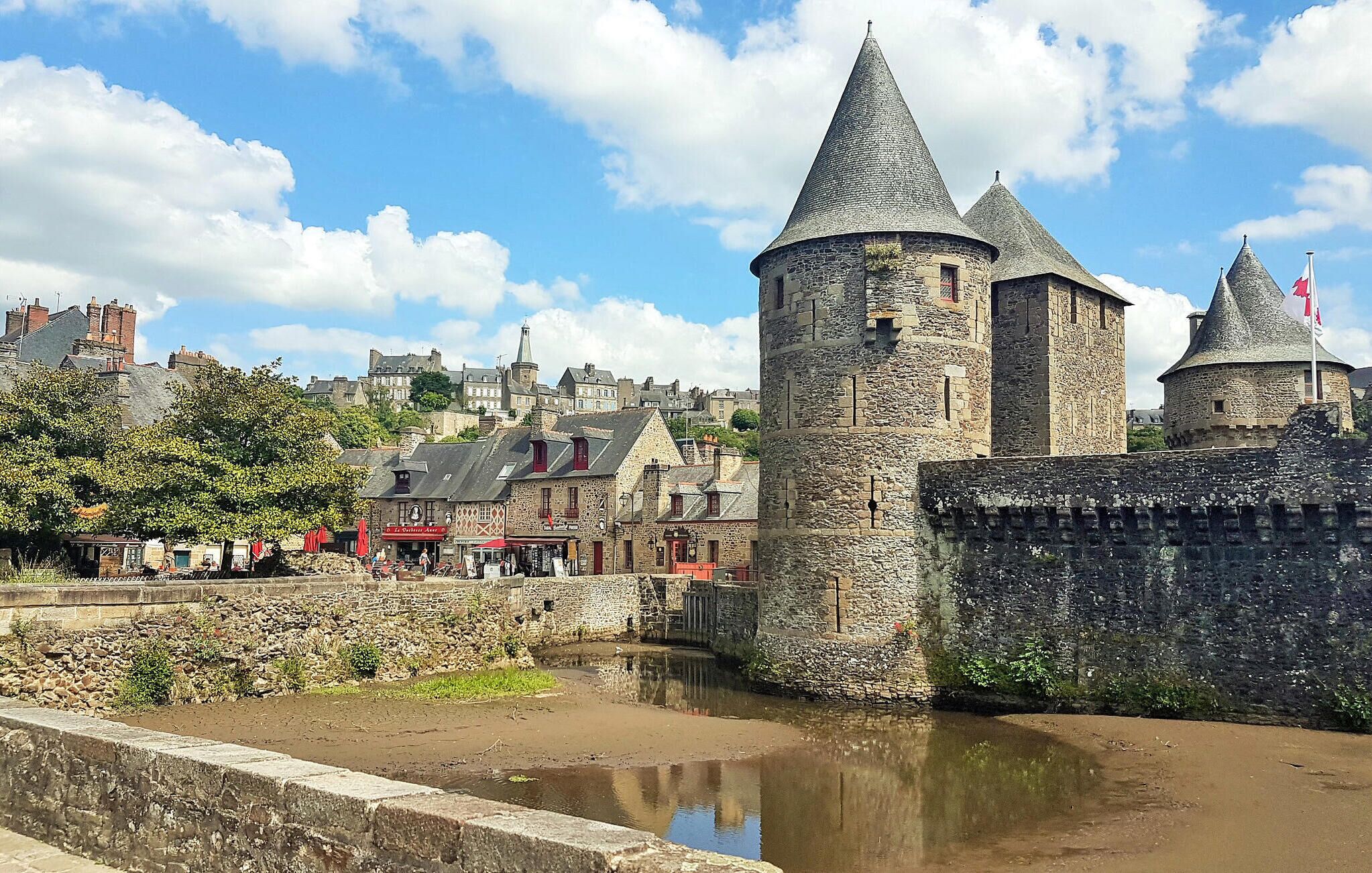 Une tour de pierre historique, surmontée d’un toit conique, qui fait partie d’une structure fortifiée entourée de douves.