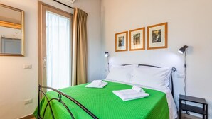 A hotel room with a green bedspread, a metal bed frame, a bedside table with a lamp, and three framed pictures on the wall.