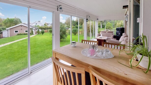 A conservatory with a wooden table, chairs, and a view of a green garden.